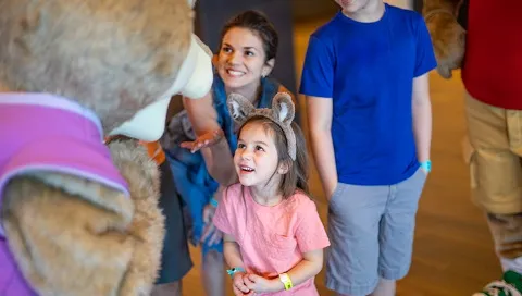 A girl wearing wolf ears looks up at a Great Wolf Lodge character.