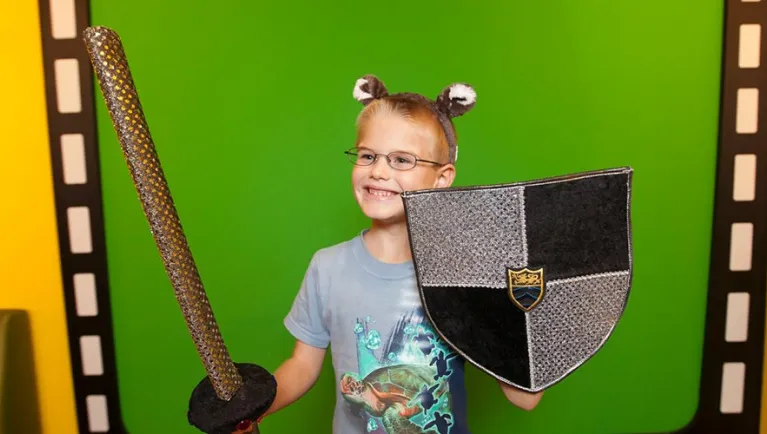 A boy in wolf ears, a sword, and shield poses for a picture 