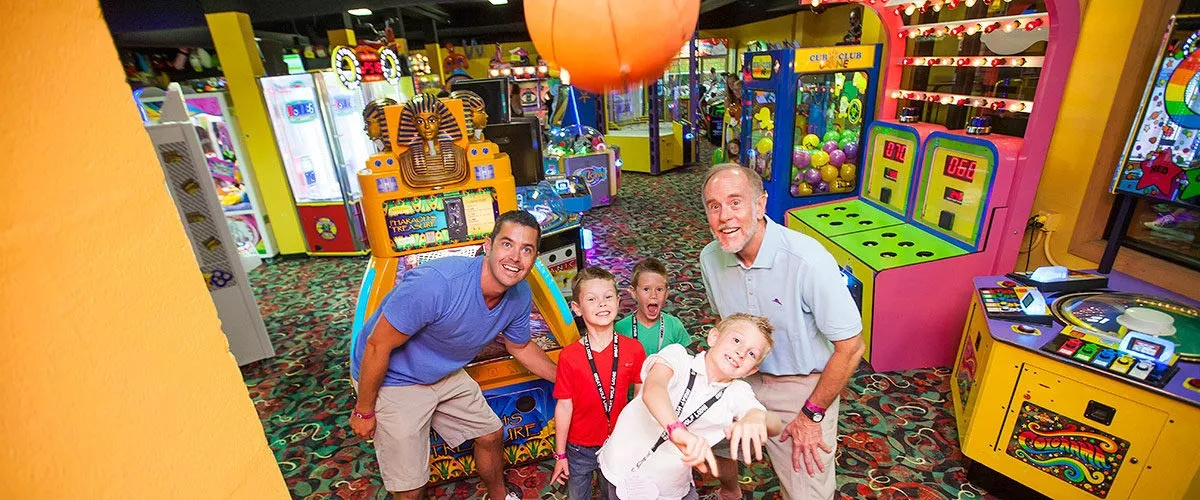 A child shoots a basketball toward a basket with his family at an arcade