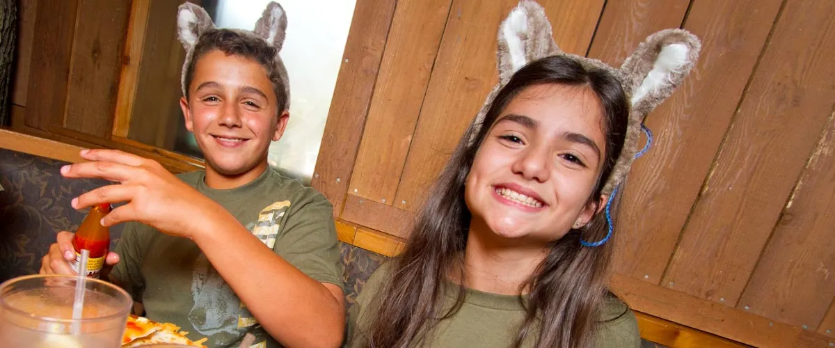 Two children wearing wolf ears having a meal smile at the camera