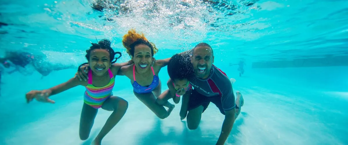 A family of four smiles at the camera while underwater in a pool