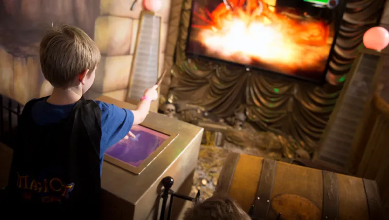 A boy points his wand at a screen as he plays MagiQuest