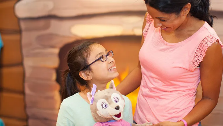 A girl holding her plush wolf toy smiles up at her mom at Great Wolf Lodge indoor water park and resort.