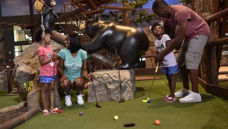 A family of four plays a round of mini golf at Great Wolf Lodge indoor water park and resort.