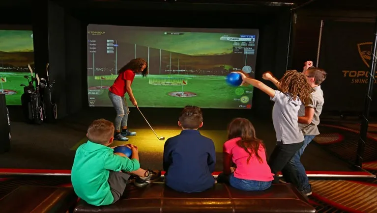 Girl lines up putter for virtual golf game and other children cheer her on
