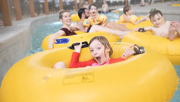A girl float down the lazy river excitedly in her inner tube