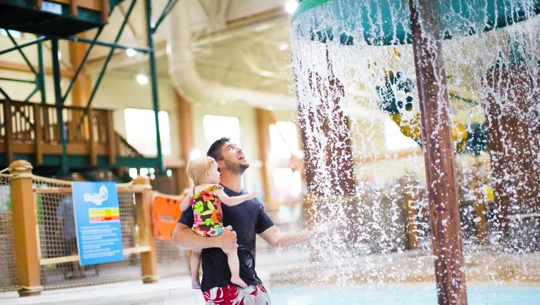 A father and toddler having fun at Cub Paw Pool located in a Great Wolf Lodge indoor water park and resort.