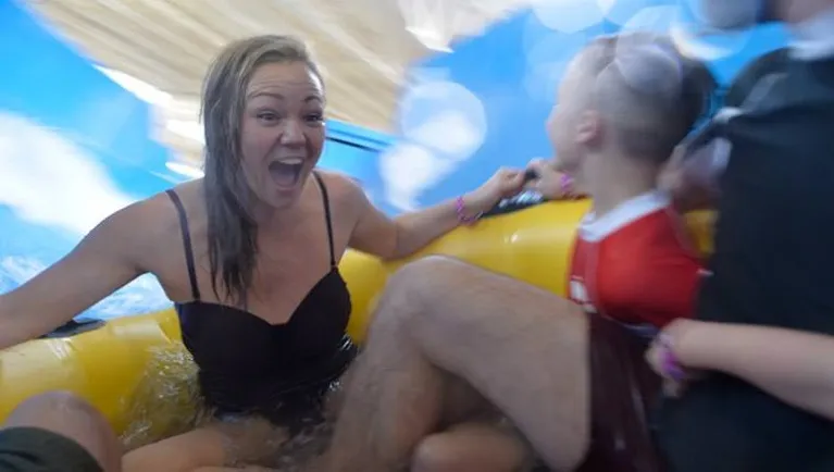 A laughs and smiles at her family as they share a tube down the Double Whirlwind water slide at a Great Wolf Lodge indoor water park.