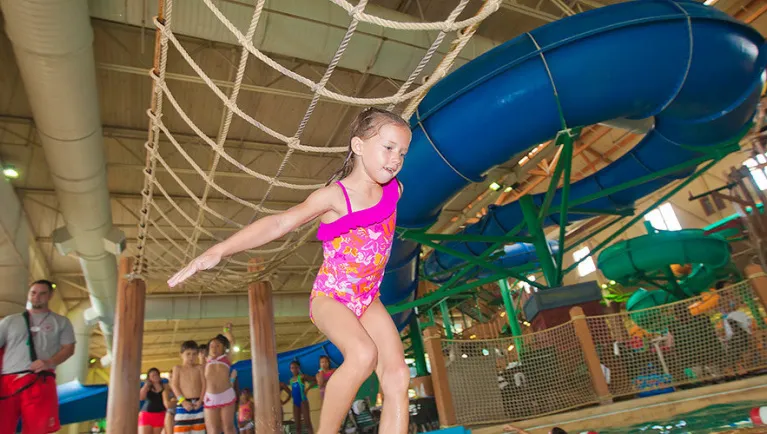A girl balances herself on a cargo net in the Frog Bog Log Walk pool at Great Wolf Lodge indoor water park and resort.