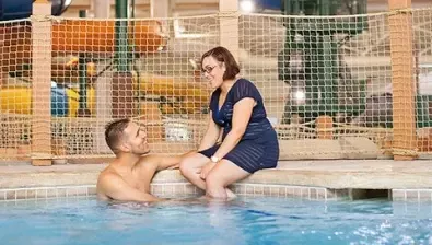 A couple relax by the Northwoods Springs pool at Great Wolf Lodge indoor water park and resort.