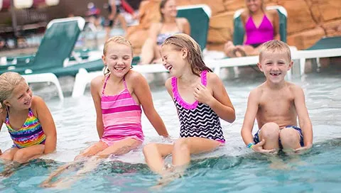 Four kids relax at the edge of an outdoor pool at Great Wolf Lodge indoor water park and resort.