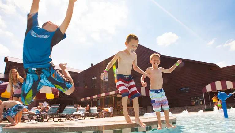 Three boys jump into an outdoor pool at Great Wolf Lodge indoor water park and resort.