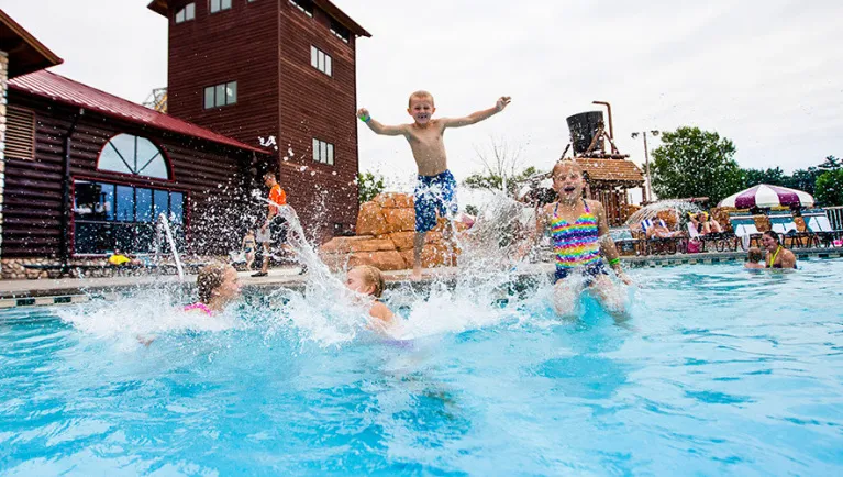 Four kids jump into an outdoor pool at Great Wolf Lodge indoor water park and resort.