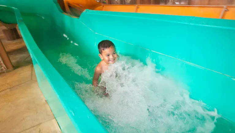 A boy smiles as he rides a water slide