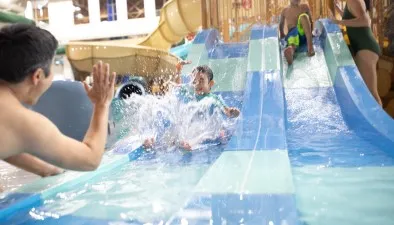 A father reaches down toward his child as he finishes a water slide