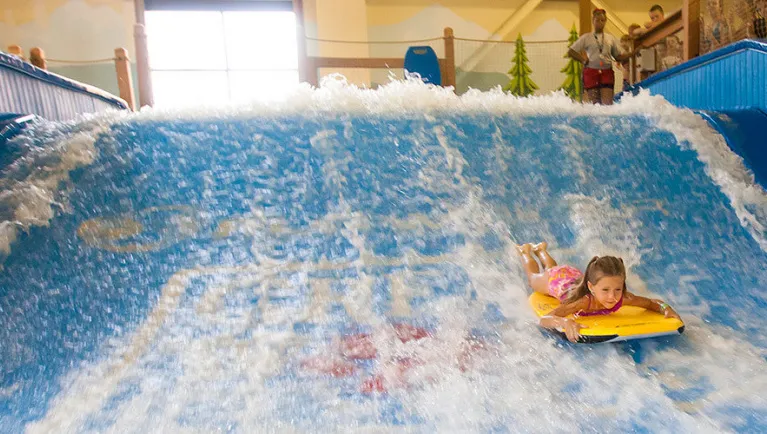 A girl balances on a bodyboard on Wolf Rider Wipeout at Great Wolf Lodge indoor water park and resort.